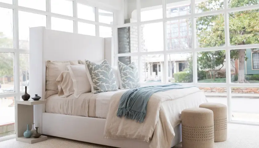A light blue throw with fringe adds a cozy touch to this serene bedroom, draped over a bed with linen bedding.