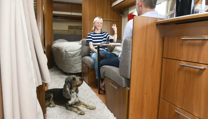 Un enfant et un homme discutent dans un camping-car, un chien au sol. Une astuce chauffage camping-car pour un voyage confortable.