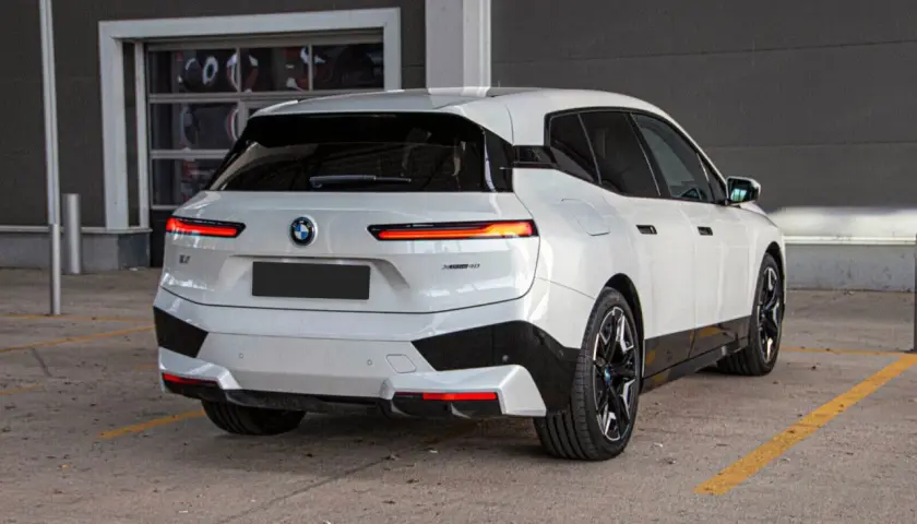 Białe BMW iX z czarnymi akcentami stoi na parkingu.