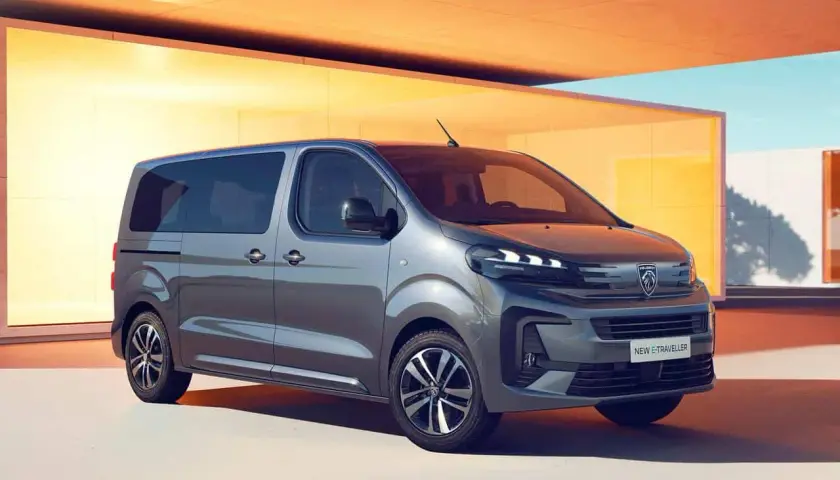 Nowy Peugeot e-Traveller, szary van, zaparkowany przed nowoczesnym budynkiem z żółtymi akcentami.