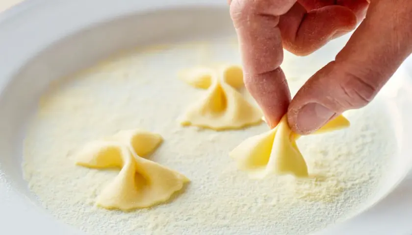 Hand formt Farfalle-Nudeln in einer Schüssel mit feiner farina di semola.