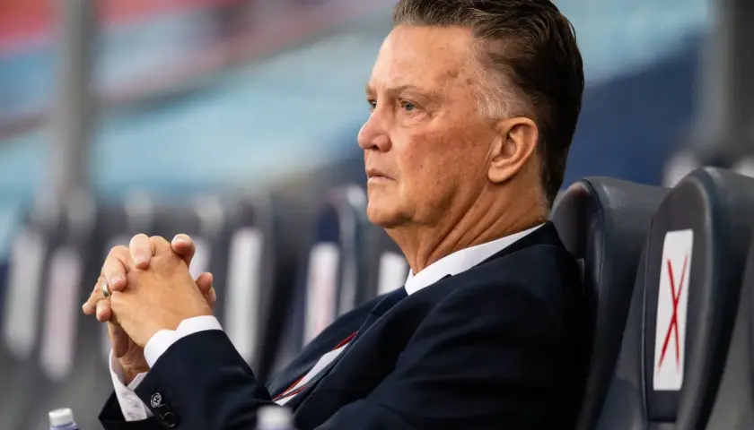 Louis van Gaal, znany z prowadzenia drużyny z pasją, siedzi z zamyślonym wyrazem twarzy, dłonie splecione.