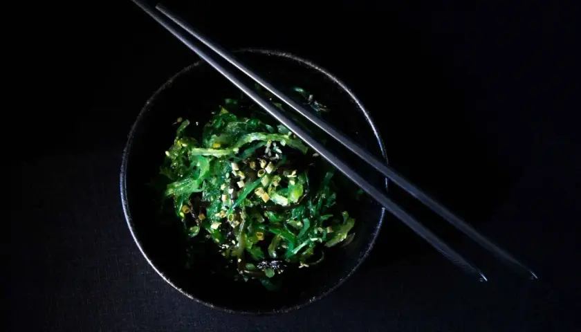 Insalata di wakame, un piatto ricco di **wakame proprietà** benefiche, guarnita con semi di sesamo e cipollotto, pronta per essere gustata con le bacchette.