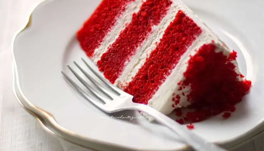 Una fetta di torta Red Velvet, con strati rossi e crema bianca, pronta per essere gustata. La ricetta perfetta per un dolce indimenticabile.