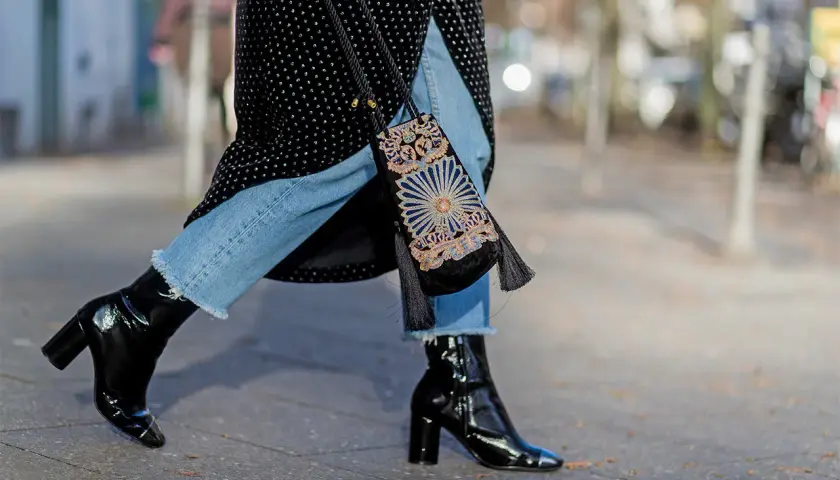 Estilo urbano: cómo combinar botines negros brillantes con jeans desgastados y un bolso bordado.