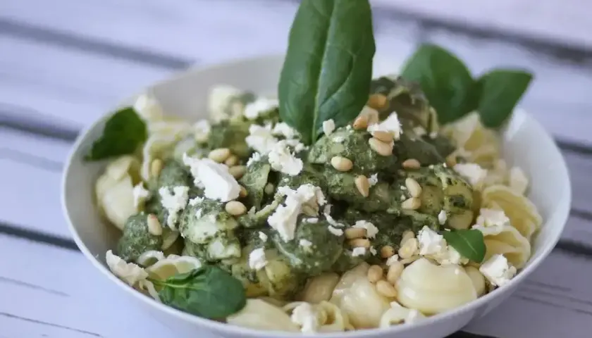 Pyszny makaron z fetą, polany zielonym pesto i posypany orzeszkami pinii. Idealny na szybki obiad.