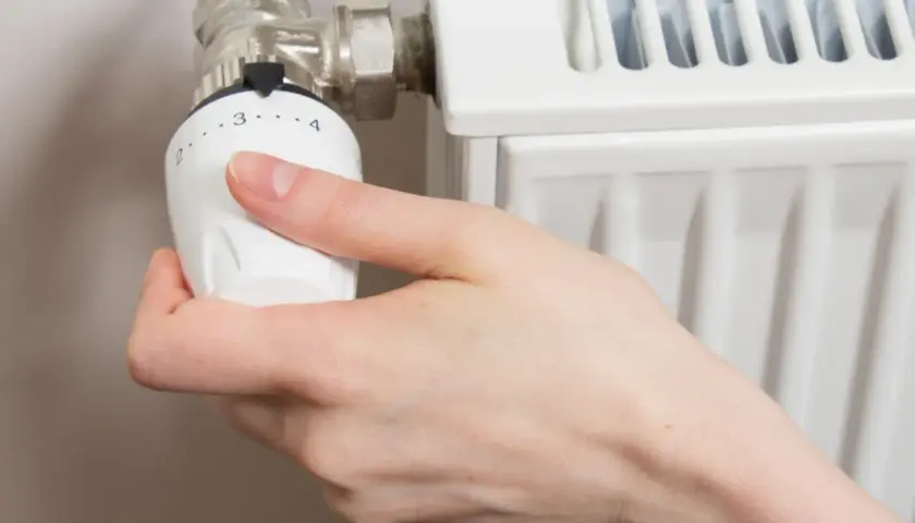 Mano girando la perilla del radiador hacia la izquierda para cerrarlo.