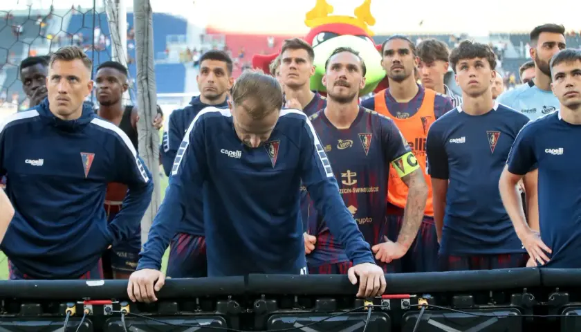 Piłkarze Pogoni Szczecin w granatowych strojach stoją w rzędzie, patrząc w dół.