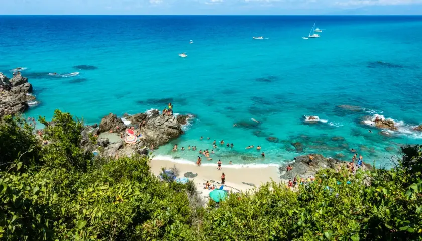 Spiaggia con acque cristalline e gente che nuota e prende il sole. Un luogo ideale per il tuo prossimo viaggio in Calabria mare dove andare.
