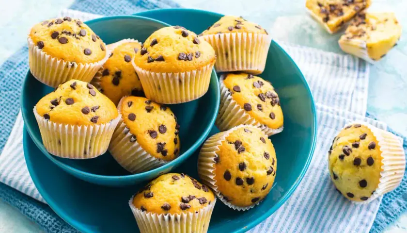 Muffin con gocce di cioccolato, dorati e invitanti, serviti in una ciotola blu. Perfetti per una pausa golosa.