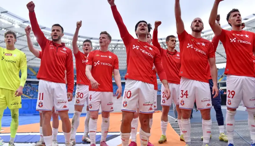 Piłkarze Wisły Kraków świętują, podnosząc ręce w geście triumfu. Ich stroje sugerują, że to ważny moment, być może związany z udanymi transferami.