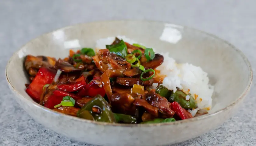 En skål med ris och en smakrik kyckling cashew-röra med paprika, champinjoner och salladslök.