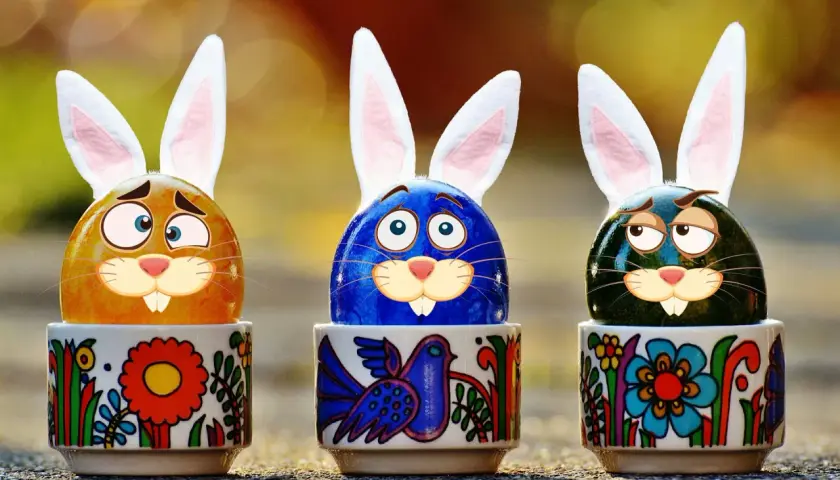 Trzy pisanki z króliczymi uszami w ozdobnych kieliszkach. Zastanawiają się, ile trwa Wielkanoc w Niemczech.