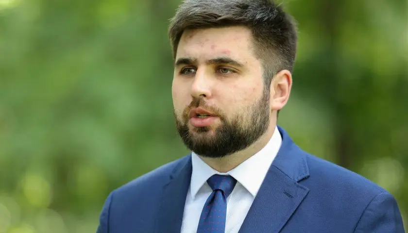 Młody mężczyzna w garniturze, Jakubas Banaszek, budzi zaskoczenie działaczy swoją kandydaturą na premiera.