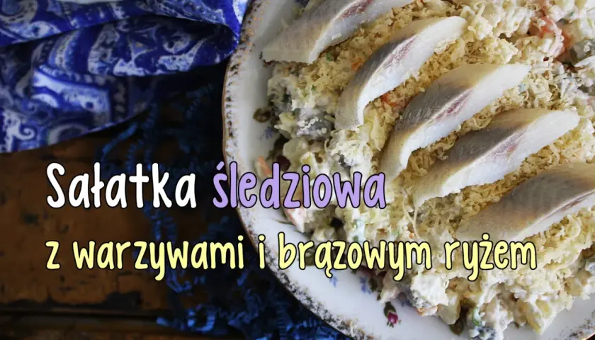 Sałatka śledziowa z warzywami i brązowym ryżem, ozdobiona kawałkami marynowanych śledzi.