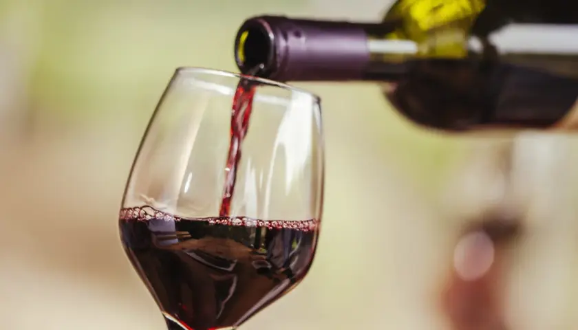 Czerwone wino nalewane do kieliszka. Widoczne "łzy" na ściance, świadczące o zawartości alkoholu.