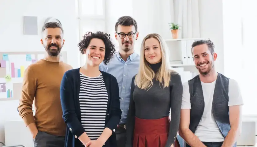 Fünf lächelnde Personen stehen im Büro. Sie haben erfolgreich ihr Fernstudium anerkannt und feiern ihren Erfolg.