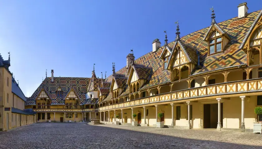 Cour intérieure des Hospices de Beaune, un joyau architectural à visiter. Toits colorés, arcades et pavés de pierre.