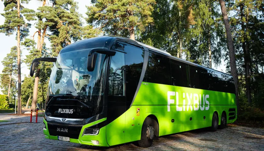 Zielony autokar Flixbus zaparkowany na brukowanym placu, otoczony drzewami.