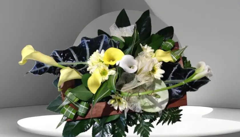 Composition florale élégante avec des arums blancs et jaunes, des feuillages sombres et des petites fleurs blanches.