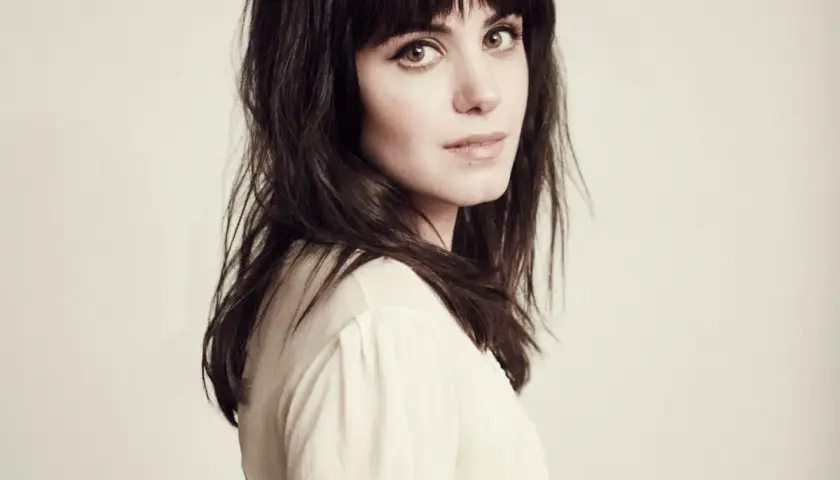 Katie Melua, jakby śpiewała "I Will Be There", z ciemnymi włosami i przenikliwym spojrzeniem.