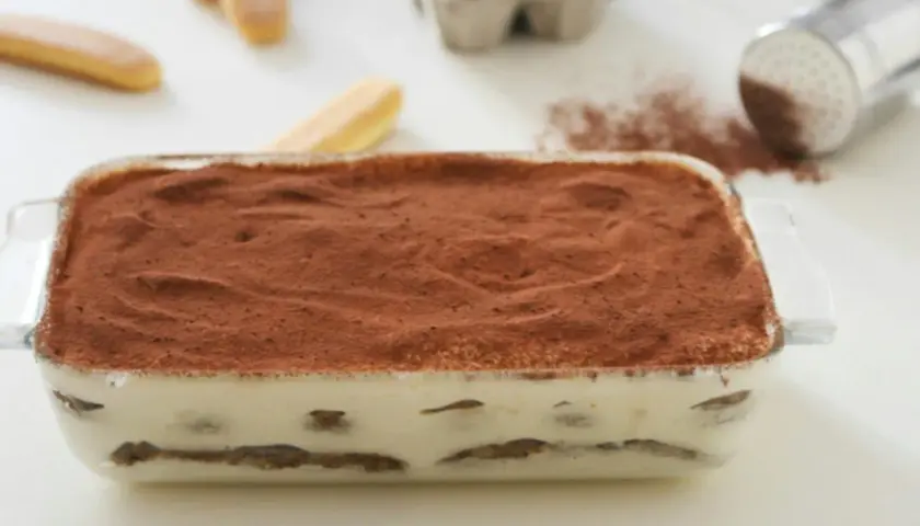 Tiramisù pronto in teglia, con strati di savoiardi e crema al mascarpone, spolverato di cacao. La ricetta perfetta per un dolce goloso.