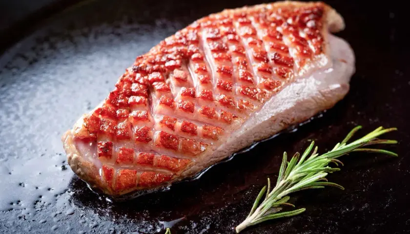 Magret de canard à la poêle, peau dorée et croustillante, avec une branche de romarin. Le temps de cuisson est idéal pour un plat savoureux.