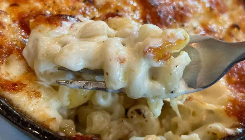 Un tenedor levanta una porción cremosa de macarrones con queso horneados, con la parte superior dorada y burbujeante.