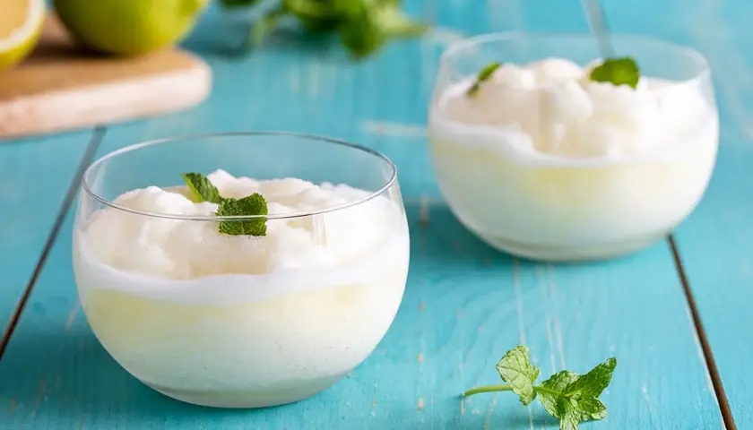 Due bicchieri di sorbetto al limone senza albume, guarniti con menta fresca, su un tavolo di legno blu.