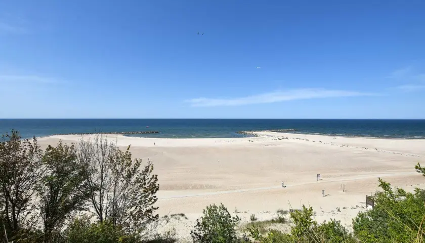 Szeroka, piaszczysta plaża w Jarosławcu, z łagodnymi falami Bałtyku i zielenią w tle. Idealne miejsce na relaks i podziwianie widoków, oferujące liczne atrakcje.