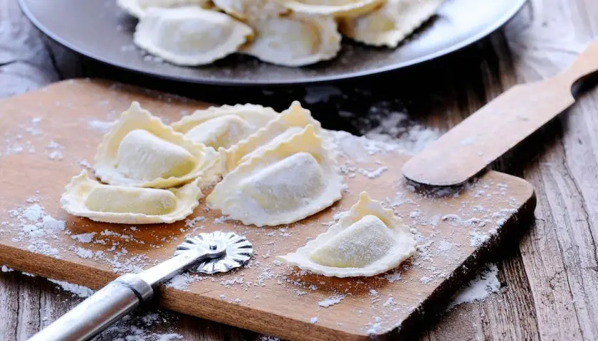 Raviolis frais sur une planche à découper avec une roulette à pâtisserie et une spatule.