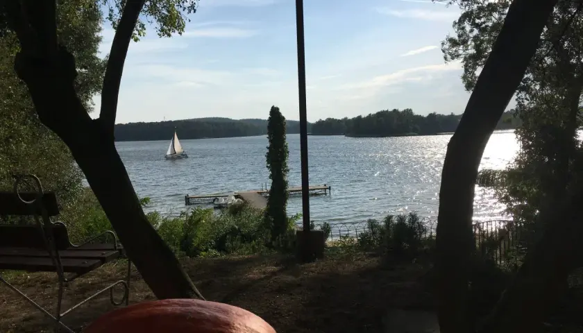 Spokojny dzień nad jeziorem w Puszczy Noteckiej. Żaglówka sunie po wodzie, a na brzegu czeka ławka i wielka dynia.