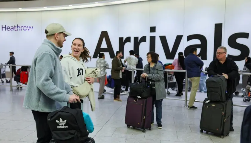 Para podróżnych z bagażami na lotnisku Heathrow, na tle napisu "Arrivals".