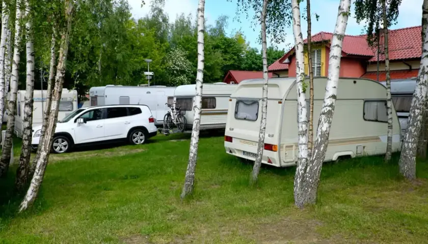 Wesoły camp Polska z przyczepami kempingowymi i białym autem, otoczony drzewami.