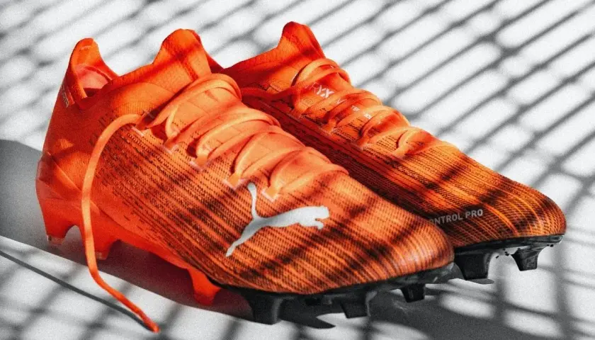 Pomarańczowe korki piłkarskie Puma z napisem "CONTROL PRO". Różnice między korkami profesjonalnymi a amatorskimi są widoczne w technologii i materiałach.
