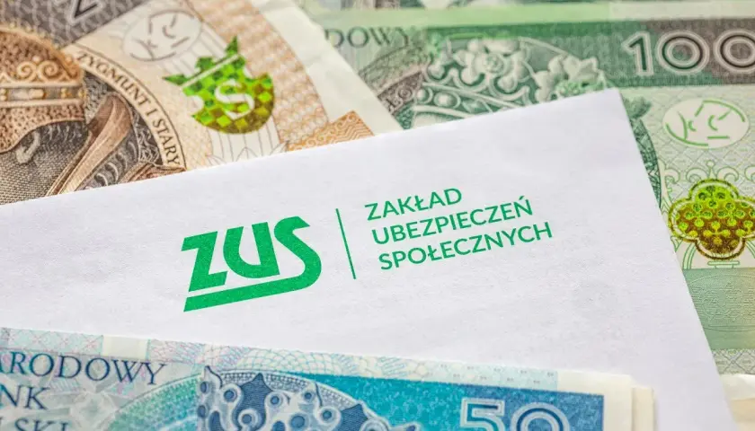 Biała koperta z logo ZUS na tle polskich banknotów. Dokumenty ZUS i pieniądze symbolizują świadczenia, np. chorobowe.