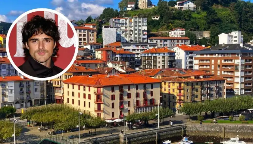 Jacob Elordi, con su aire de galán, posa sobre un pintoresco pueblo vasco con casas de tejados naranjas y un puerto lleno de barcos.