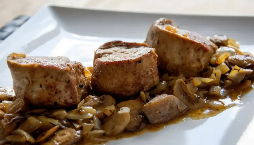 Soczyste polędwiczki w sosie pieczarkowym, podane na białym talerzu. Aromatyczny sos z pieczarkami i cebulką otula delikatne mięso.