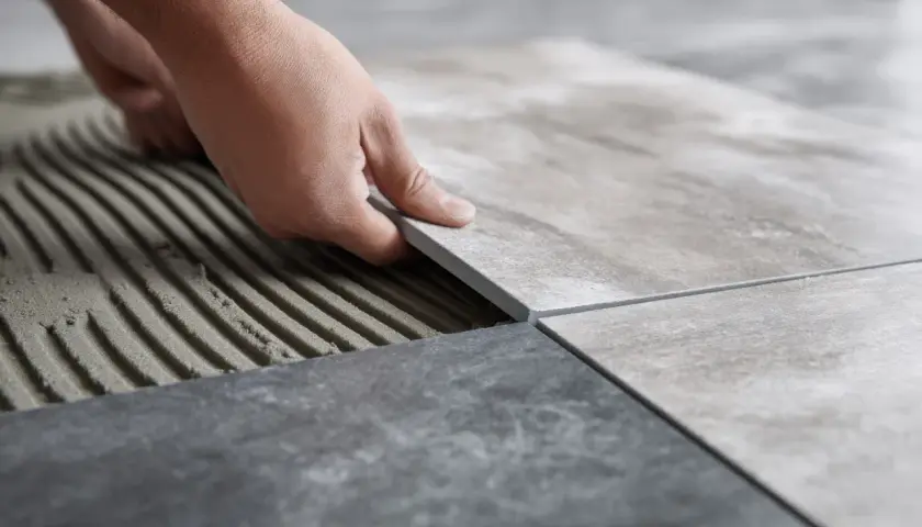 Układanie płytek 60x60. Cennik prac glazurniczych. Dłoń kładzie nową płytkę na kleju.