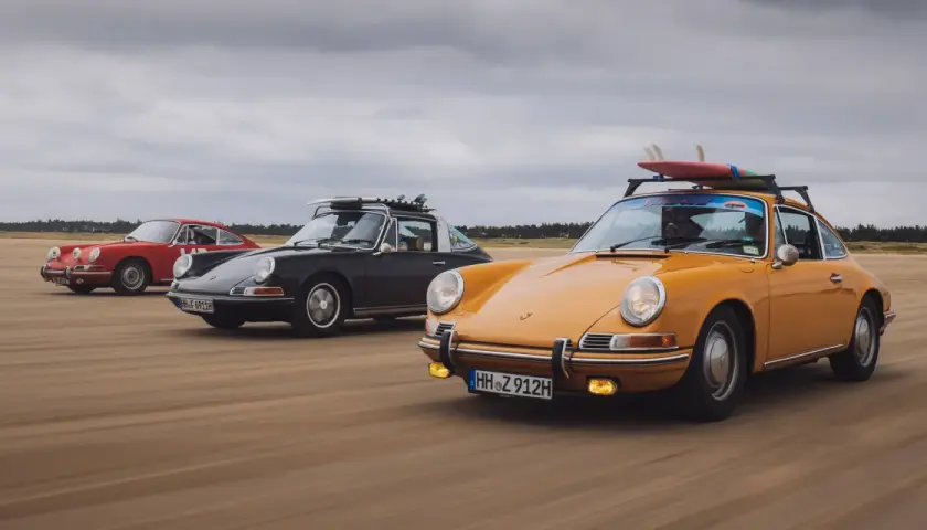 Trzy klasyczne Porsche 911 na plaży, żółte z deskami surfingowymi na dachu. Niesamowita fotografia samochodowa.