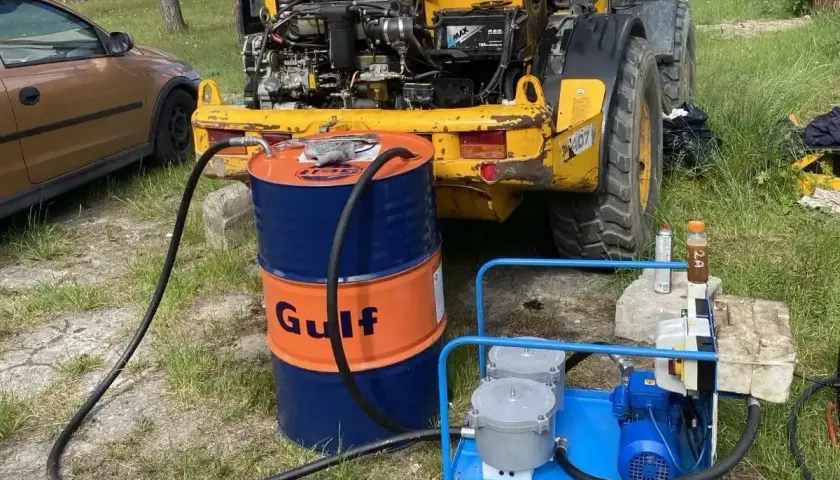 Niski poziom oleju hydraulicznego objawy: maszyna budowlana z otwartą maską, beczka Gulf, pompa.