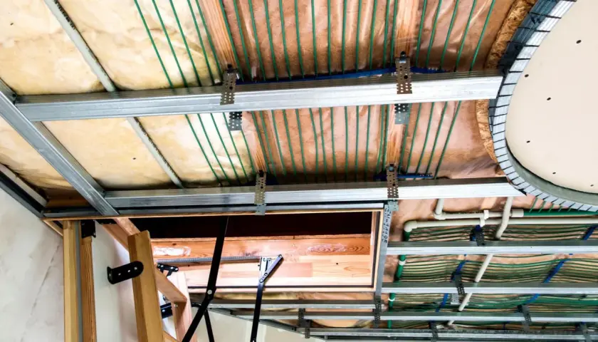 Widok sufitu podwieszanego z widocznymi instalacjami. Widać metalowe profile, wełnę mineralną, rurki systemu ogrzewania podłogowego i elementy konstrukcyjne. Maty kapilarne wady nie są widoczne.