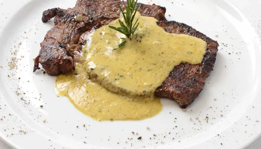 Un steak grillé, nappé d'une sauce crémeuse et garni d'une branche de romarin. Parfait pour accompagner une sauce pour entrecôte au barbecue.