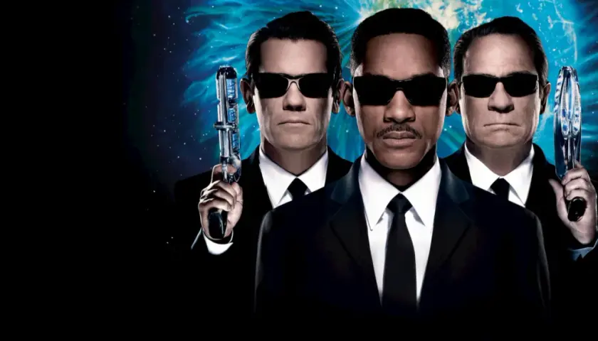 Agent J, K och O, rollistan i Men in Black 3, redo för action med sina futuristiska vapen mot en stjärnklar bakgrund.