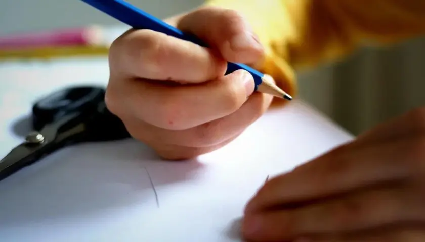 Dziecko pisze kredką, licząc ile dni do końca szkoły. Obok leżą nożyczki.