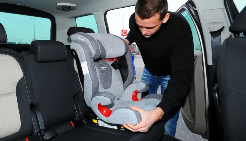 Mężczyzna montuje fotelik samochodowy na bazie Isofix. Czy baza Isofix pasuje do każdego fotelika? Sprawdźmy!