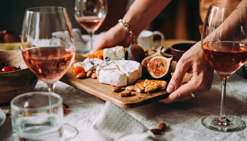 Gemütliche weinverkostung zu hause mit Roséwein, Käse, Feigen und Nüssen auf einem Holzteller.