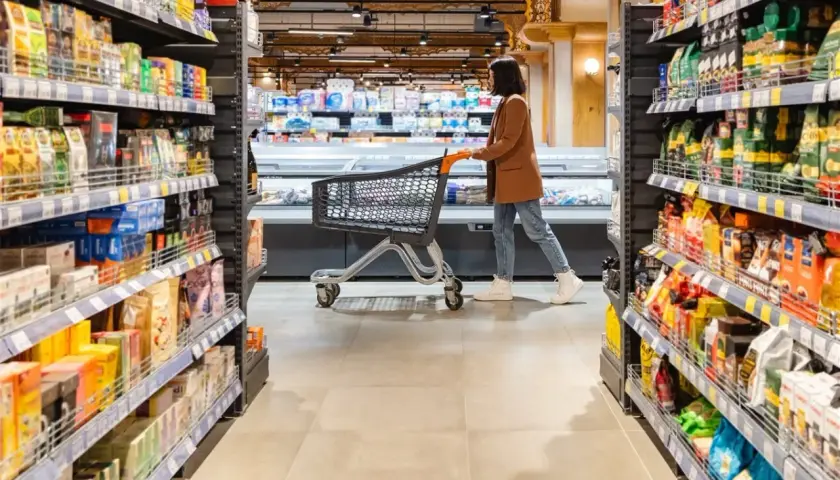 Kobieta z wózkiem w sklepie, między regałami pełnymi produktów. Może szuka jakiegoś dobrego **brendi** na prezent.