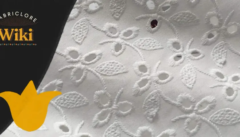 Close-up of white eyelet fabric with floral embroidery. This delicate fabric features cut-out holes surrounded by decorative stitching, creating a beautiful, airy pattern.
