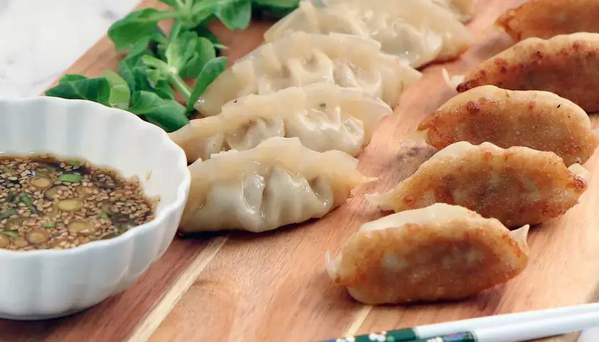 Stekta och ångade dumplings på en träbricka med dippsås och grönsaker. Ett perfekt dumplings recept för en god måltid.